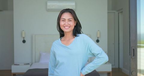 Asian woman smiling in minimalist bedroom enjoying morning sunlight and cozy atmosphere