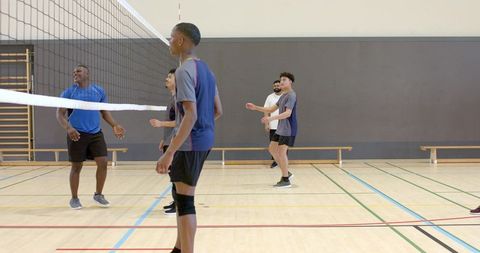 Male teammates playing indoor volleyball on wood court, teamwork and athletic training