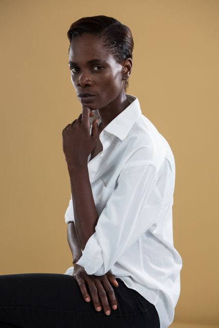 This image features an androgynous man wearing a white shirt, posing confidently against a beige background. The serious expression and minimalist style make it suitable for fashion editorials, modern lifestyle blogs, and advertisements focusing on contemporary androgynous fashion.