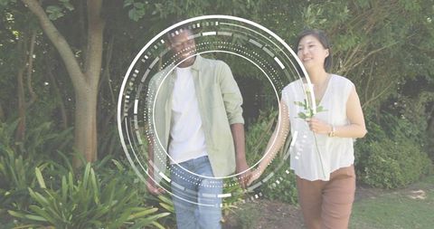 Young couple walking in green garden holding sprig with futuristic HUD overlay circles