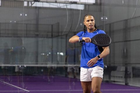 Male padel player wearing smartwatch holding paddle on indoor glass court