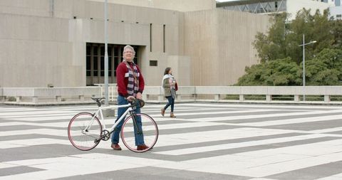 Mature man holding white bicycle and looking upward on striped urban plaza