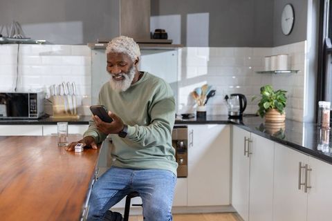 Senior african american man checking health monitor with smartphone in modern kitchen