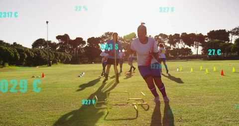 Female Soccer Players Sprinting Through Hurdle Drill on Grass Pitch at Golden Hour Training