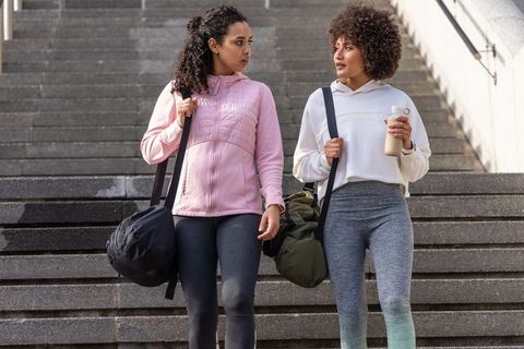 Walking and chatting diverse women in activewear carrying gym duffels on urban stairs