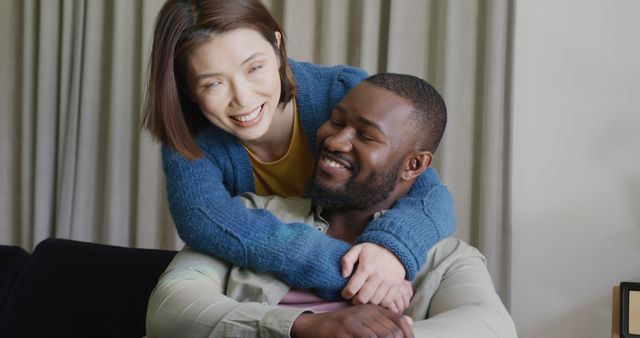 Middle-aged interracial couple embracing and smiling within home environment. Ideal for content related to relationships, diversity, love and companionship, and advertising for home products or lifestyle promotions.