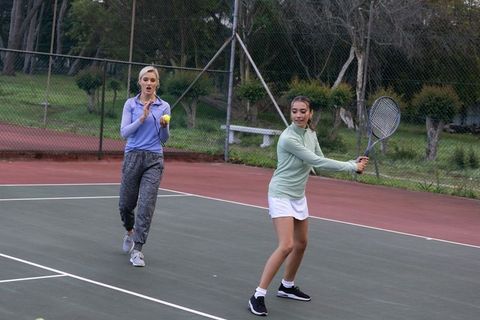 Female tennis partners practicing backhand and coaching on outdoor park court