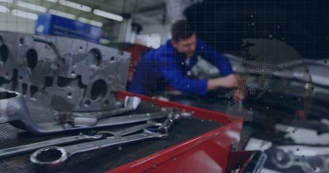 Mechanic tightening engine bolts in engine bay with red tool cart in busy workshop