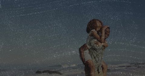 Couple enjoying piggyback walk along sandy shore laughing and embracing by ocean