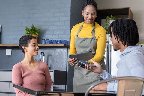Barista accepting contactless payment with tablet and card reader from African American couple