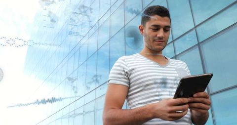 Young professional using tablet outdoors with digital data overlays on glass office facade