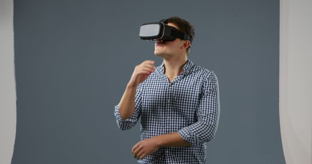 Young man using a virtual reality headset experiencing virtual environments. Ideal for illustrating concepts of modern technology, digital innovation, virtual reality, and gaming. Use in technology blogs, presentations on VR advancements, or advertisements for tech devices.