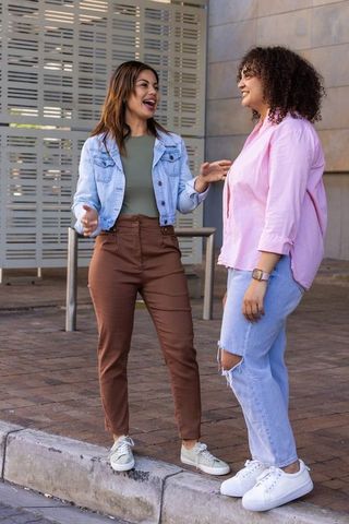 African american friends chatting and laughing on urban curb near modern building