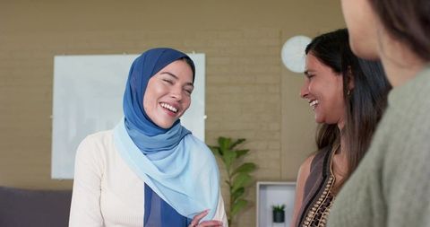 Laughing woman wearing two-tone blue hijab chatting with colleagues during casual office meeting