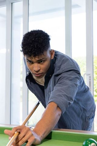 Focused african american teen aiming cue playing pool in sunlit home