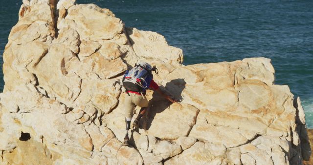 Man climbing a rocky cliff overlooking the ocean. Perfect for themes related to adventure, extreme sports, outdoor activities, thrill seeking, and determination. It can be used in magazines, travel blogs, sports websites, or advertisements promoting outdoor gear.