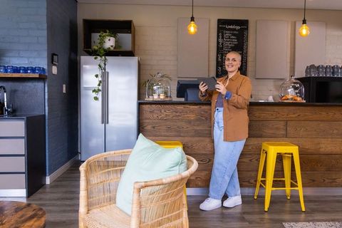 Cafe owner using tablet behind rustic wooden counter in modern coffee shop interior