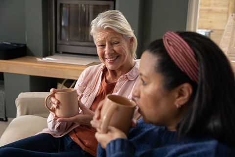 Senior and mature friends sharing coffee and conversation on cozy living room sofa