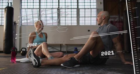 Sitting, chatting during cooldown at industrial gym with fitness data overlays 2002-2021