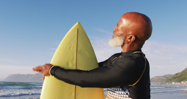 Senior african american man walking with a surfboard at the beach. healthy outdoor leisure time by the sea.