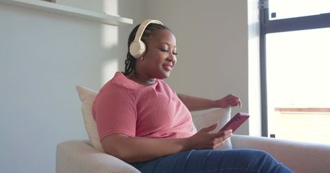 African american woman relaxing with headphones and smartphone in bright cozy living room