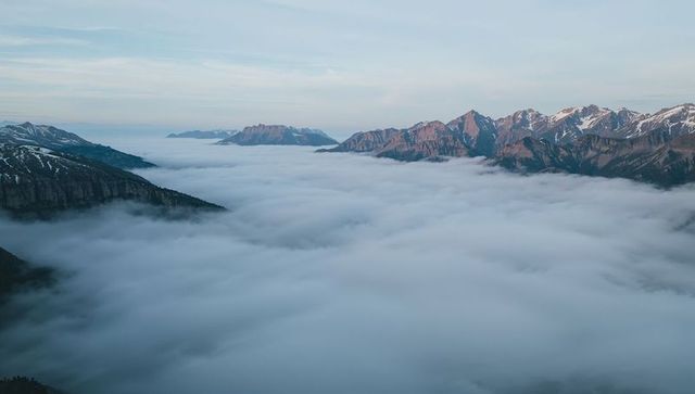 Low-Lying Clouds Filling Alpine Valley with Snow-Patched Peaks and Pale Morning Sky