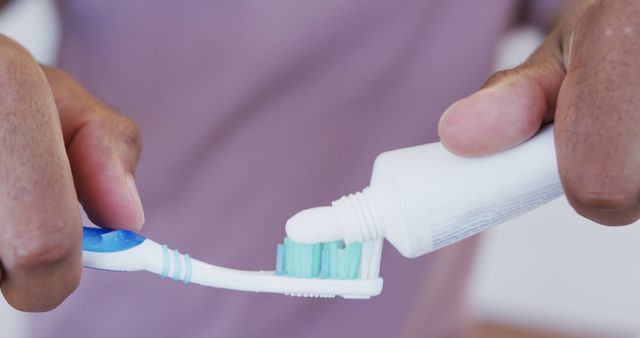 Hands squeezing toothpaste onto toothbrush in a close-up view. Suitable for depicting oral hygiene, dental care advertisements, health and wellness articles, morning routine illustrations, and personal hygiene tutorials. Perfect for health guides, dental care promotions, or personal care product marketing.