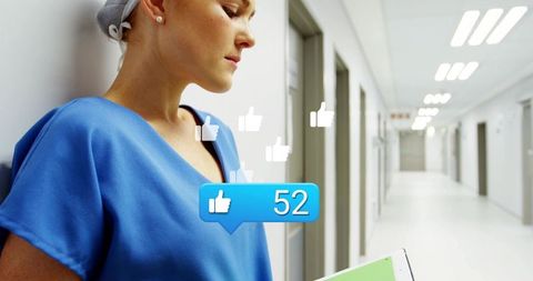 Nurse leaning in hospital corridor holding tablet receiving social media thumbs-up overlay