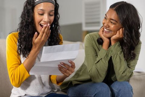 Diverse mother and teenage daughter reacting joyfully to surprise letter on couch