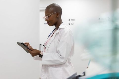 Clinician using tablet in radiology corridor checking mri and ct signs wearing lab coat