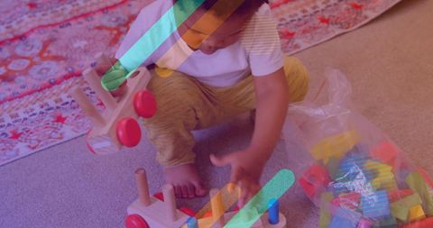 Toddler reaching for peg toy while holding wooden car with red wheels on cozy rug