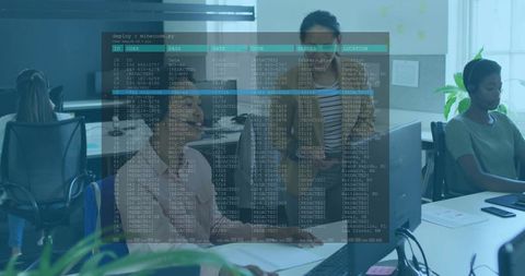 Two women collaborating at office monitor with terminal overlay, teamwork and data analysis