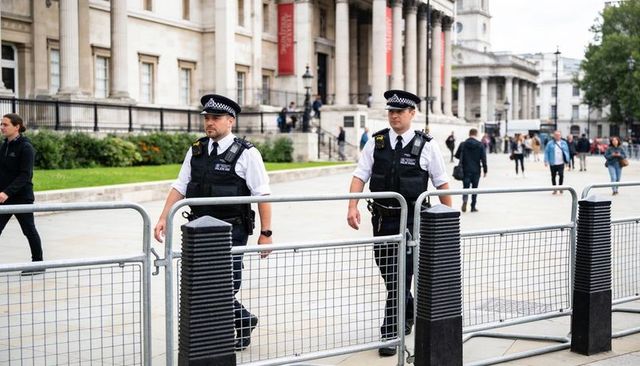 Uniformed police officers patrolling historic city plaza passing crowd-control barriers