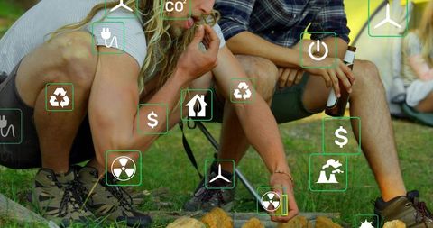 Friends camping and building campfire on grassy campsite with energy sustainability icons overlay