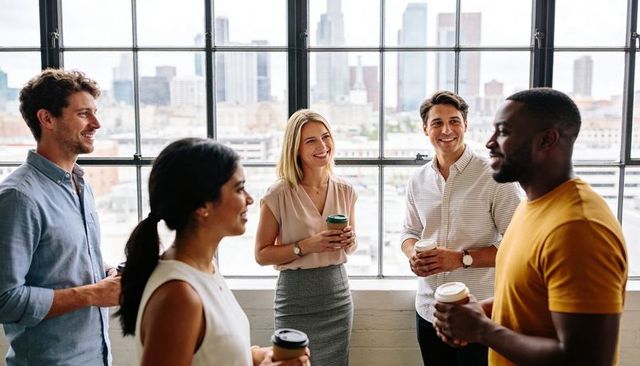 Coworkers chatting over coffee in modern office with large window and city skyline
