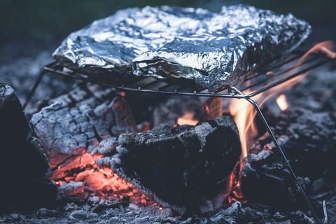 Foil-wrapped meal cooking over campfire grate with ember glow