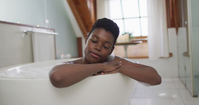 Portrait of african american attractive woman relaxing in foam bath and smiling in bathroom. beauty, pampering, home spa and wellbeing concept.