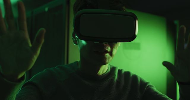 Person using VR headset within environment illuminated by green light. Could be used to represent advanced technology, gaming, futuristic environments, or promotional materials for virtual reality experiences.