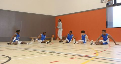 Basketball Players Stretching Under Coach's Guidance in Gym