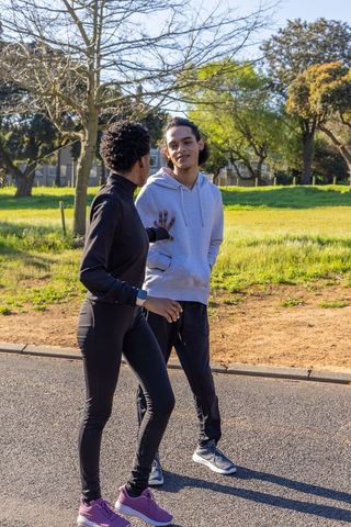 Diverse friends walking and talking in neighborhood park showing smartwatch and fitness
