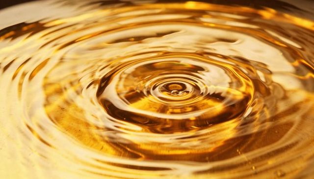 Golden liquid droplet creating concentric ripples macro reflection and texture