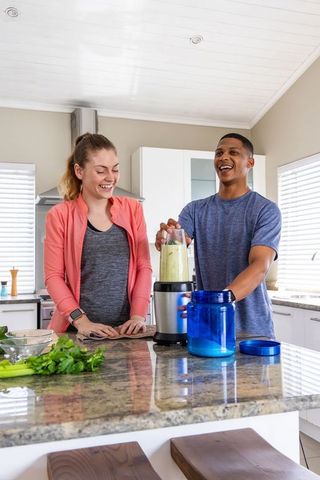 Energetic couple making green smoothie on granite kitchen island