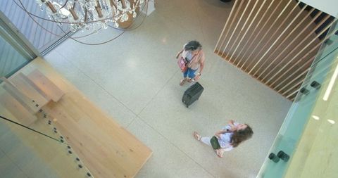 Overhead travelers standing in modern hotel lobby holding suitcase under chandelier