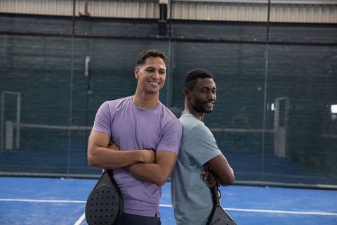 Confident padel duo standing back-to-back on indoor blue court holding rackets