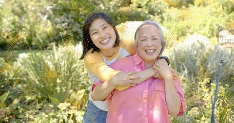 Smiling daughter hugging mother in sunlit garden, family bonding outdoors