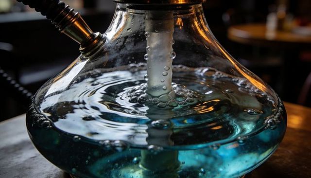 Bubbling hookah base revealing central stem in teal water reflecting warm lounge light