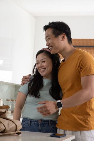 Asian couple smiling and embracing in contemporary kitchen, natural light home moment