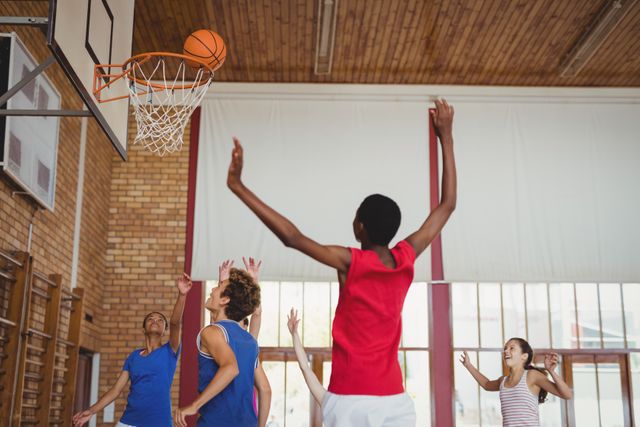 High school kids playing basketball in a gymnasium, showcasing teamwork and athleticism. Ideal for use in educational materials, sports promotions, youth activity campaigns, and fitness-related content.