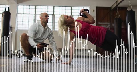 Woman performing kettlebell side plank while trainer monitoring performance data overlay