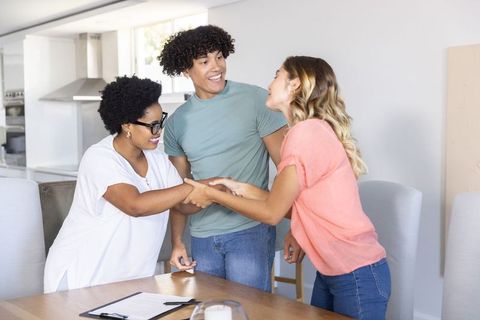 Multiracial friends shaking hands during casual home meeting at sunlit dining table
